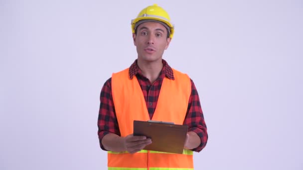 Young happy Hispanic man construction worker showing clipboard and giving thumbs up - Felvétel, videó