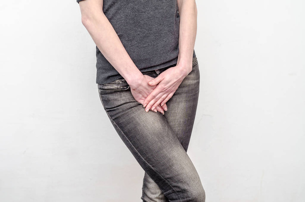 Young slim girl in jeans holds hands pressed between her legs. W - Φωτογραφία, εικόνα