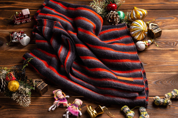 knitted scarf in black and red stripes and christmas decorations on a wooden background - Photo, image