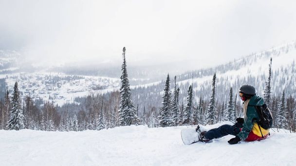 Snowboarderin sitzt in den Bergen auf einer schneebedeckten Piste. - Foto, Bild