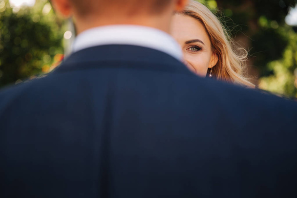 Brides half of the face is hidden behind the back of the groom - 写真・画像