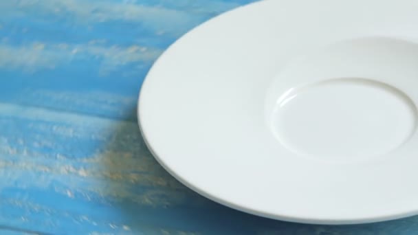 Zbliżenie białego talerza obracającego się na niebieskim stole. - Materiał filmowy, wideo