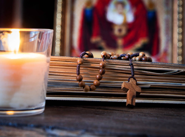 The time for prayer. Wooden Rosary on an ancient prayer book. Icon of the Mother of God and Jesus. Lighted candle - Fotó, kép