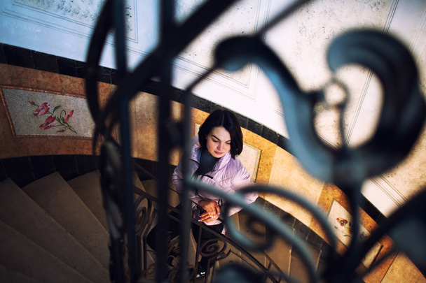 Νέα όμορφη γυναίκα στέκεται σε παλιά στρογγυλό σπειροειδές σκάλα. - Φωτογραφία, εικόνα