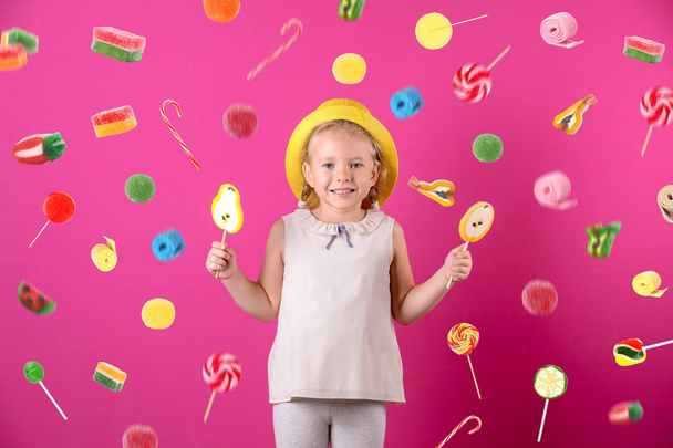 Adorable little girl with lollypops and flying candies on color background - 写真・画像