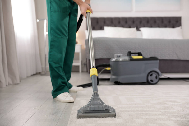 Professional janitor removing dirt from carpet with vacuum cleaner in bedroom, closeup. Space for text - Fotografie, Obrázek