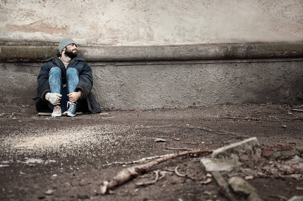 Poor homeless man sitting near wall on street. Space for text - Фото, зображення