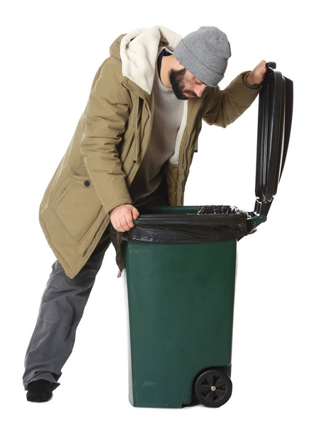 Poor homeless man digging in trash bin isolated on white - Photo, image