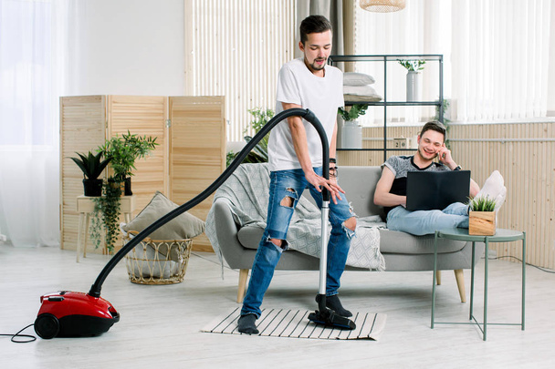 Happy gay man cleaning home, dancing with vacuum cleaner and having fun. Housework, chores concept - Photo, image