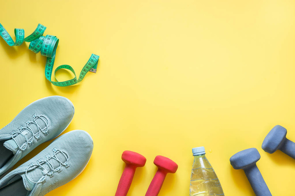 Fitness set with dumbbells,measuring tape, fitness shoes,bottle of water on yellow. - 写真・画像