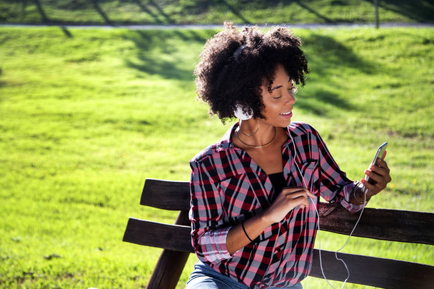 Akıllı telefon tutan gülümseyen genç çekici Afro-Amerikan kadın Closeup portre, selfie fotoğraf çekmek ve arka planda bulanık bitkiler ile parkta ayakta - Fotoğraf, Görsel