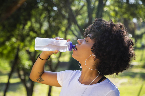Fitness african model with a water bottle in the park. - Foto, imagen