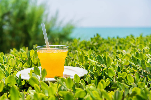 summer, a glass of fresh juice from yellow tropical fruits on the beach, on green grass, against the background of the sea - Fotografie, Obrázek