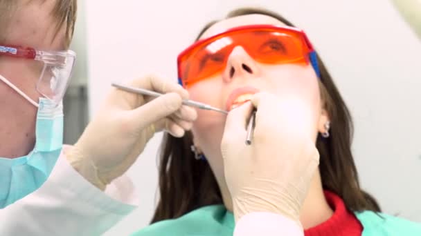 Női beteg az orvos megvizsgálja őt a fogorvosi rendelőben, fogászati ellátás fogalmát próbálja. Média. Egy fiatal lány, védő szemüveg, ül a székre, fogorvos látogatás. - Felvétel, videó