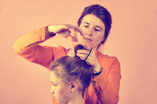 Young mother doing her baby's hair on a pink background. - 写真・画像