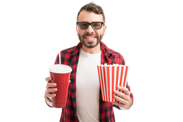 schöner und glücklicher Mann hält Popcorn und Limo in der Hand, während er sich 3D-Film im Studio ansieht - Foto, Bild