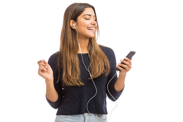 Молода стильна жінка носить навушники під час використання телефону на білому тлі
 - Фото, зображення