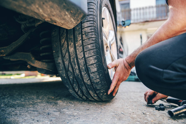 Close up of auto mechanic changing tire while crouching at workshop. - Photo, image