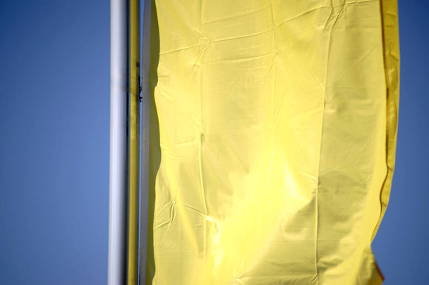 Waving flag close-up / The closeup of a yellow waving banner in front of blue sky background - Photo, Image