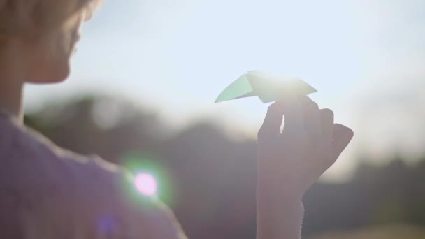 Una chica joven y hermosa con un tatuaje en la mano lanza un avión de papel. Mujer bonita, al aire libre en la naturaleza, al atardecer, lanza un avión de papel de color
. - Imágenes, Vídeo