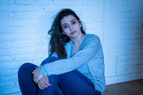 Portret młodej rozpaczliwej Łacińskiej kobiety, która czuje się nieżałosna, samotna, beznadziejna i smutna siedzi na ziemi przed białą ścianą z kopią i nastrojowym światłem. W depresji i koncepcji zdrowia psychicznego. - Zdjęcie, obraz