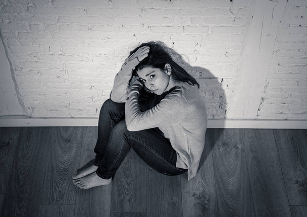 Black and white portrait of young depressed woman feeling desperate, lonely and hopeless on the ground at home. Moody light. In People women mental health, victim of domestic violence and depression. - Photo, image
