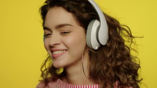 Une jeune femme écoute de la musique dans un casque. Fille heureuse dans casque sur jaune - Séquence, vidéo