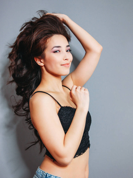 Happy sensual smiling girl asian young woman with dark long curly hair on grey wall background - Foto, Imagem