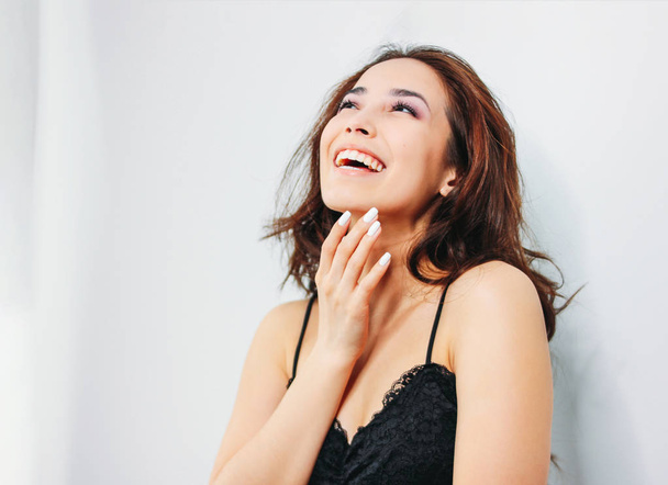 Счастливая чувственная улыбающаяся девушка азиатская молодая женщина с темными длинными вьющимися волосами в черном нижнем белье на белом фоне
 - Фото, изображение