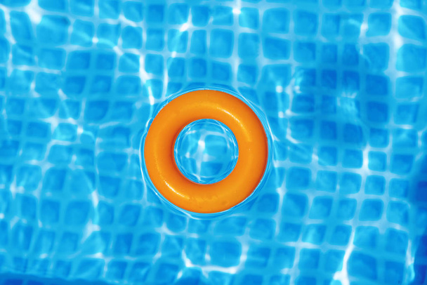 Orangefarbener aufblasbarer Ring, der an sonnigen Tagen im Schwimmbad schwimmt, Blick von oben - Foto, Bild