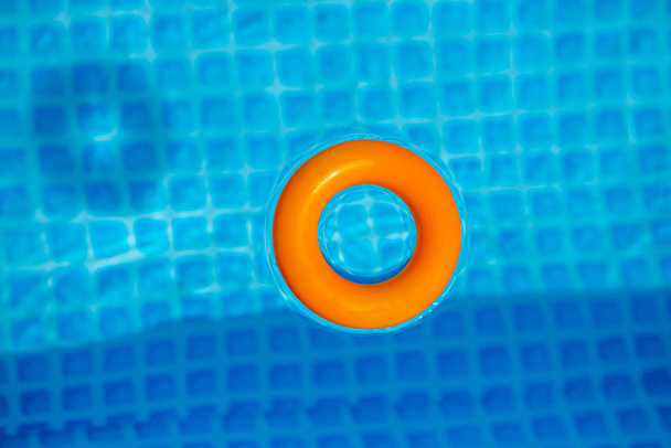 oranssi Puhallettava rengas kelluva uima-altaassa aurinkoisena päivänä, ylhäältä
 - Valokuva, kuva