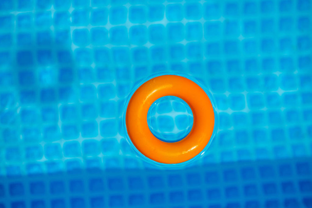 anillo inflable naranja flotando en la piscina en el día soleado, vista superior
 - Foto, Imagen