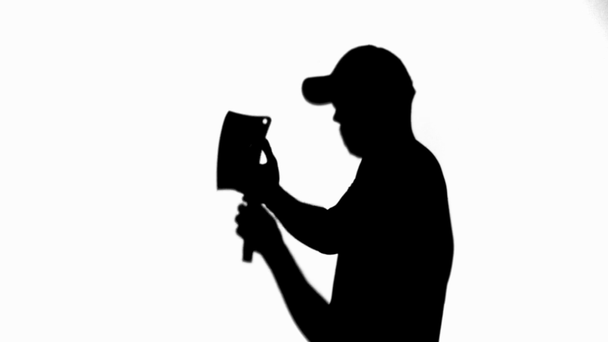 Side view of silhouette of man in cap looking at knife on white - Footage, Video