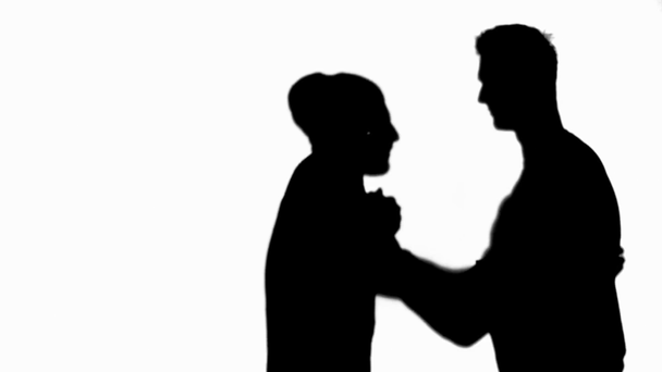 Zijaanzicht van twee silhouetten van vrienden omhelzen en schudden handen geïsoleerd op wit - Video