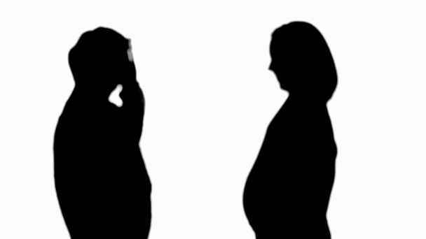 Sziluettje meglepett nő ülésén terhes lány, és hallgatta hasa izolált fehér - Felvétel, videó
