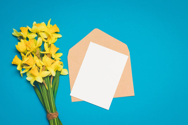 Ramo fresco de flores narcisas y el sobre con la letra sobre un fondo azul. minimalismo
 - Foto, Imagen