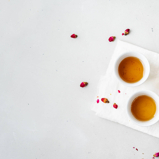 Two white ceramic cups of herbal tea with dried pink rose buds on gray background  - Foto, Imagem