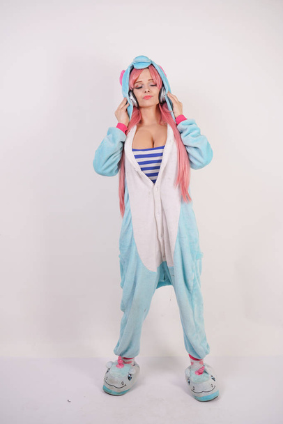 linda joven con el pelo largo de color rosa en pijama unicornio azul y zapatillas divertidas suaves sobre fondo blanco en Studio
 - Foto, imagen