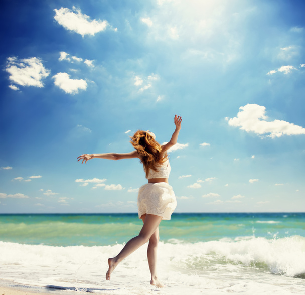 jonge roodharige meisje springen op het strand. - Foto, afbeelding