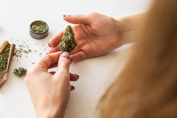 marijuana use concept. Woman rolling a cannabis blunt on white background. Woman preparing and rolling marijuana cannabis joint. Close up of marijuana blunt with grinder. - Photo, Image