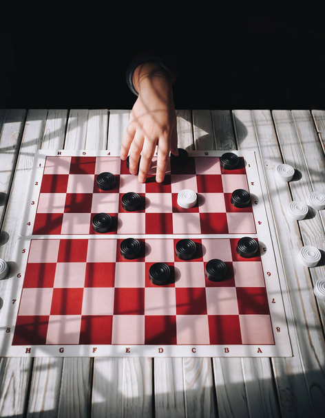 Child's hands on a checkerboard. The caucasian child plays checkers. Play board games. Loss, defeat, deadlock concept. - Photo, Image