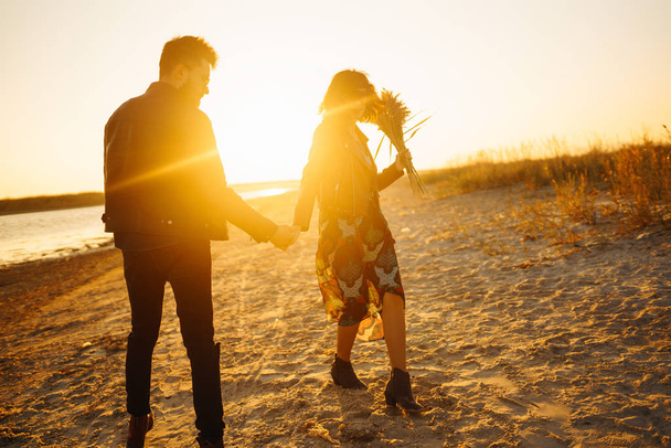 Enjoying time together.  Stylish and loving couple enjoying each other by the sea. The couple is young and in love. The concept of youth, love and lifestyle. Beautiful sunset on a summer day. - Photo, image