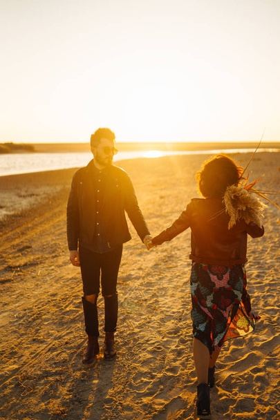 Enjoying time together.  Stylish and loving couple enjoying each other by the sea. The couple is young and in love. The concept of youth, love and lifestyle. Beautiful sunset on a summer day. - Foto, imagen