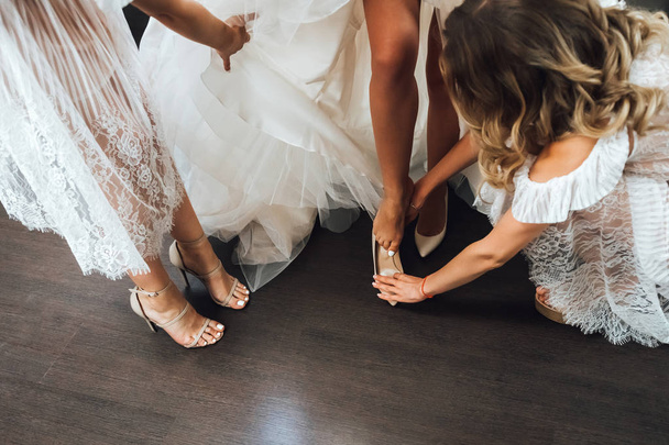 Cropped view of bridesmaids helping bride wearing shoes - Photo, Image