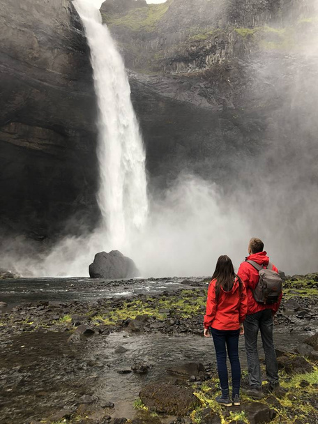 the couple looks at the beautiful Icelandic waterfall - Фото, изображение