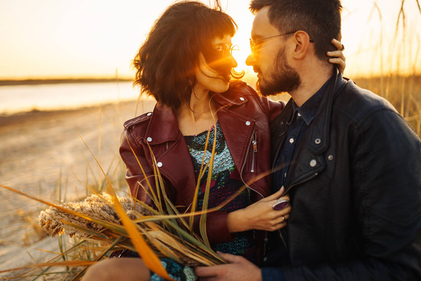 Enjoying time together.  Stylish and loving couple enjoying each other by the sea. The couple is young and in love. The concept of youth, love and lifestyle. Beautiful sunset on a summer day. - Fotografie, Obrázek