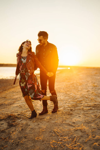 Enjoying time together.  Stylish and loving couple enjoying each other by the sea. The couple is young and in love. The concept of youth, love and lifestyle. Beautiful sunset on a summer day. - Foto, imagen
