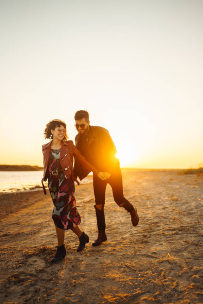 Enjoying time together.  Stylish and loving couple enjoying each other by the sea. The couple is young and in love. The concept of youth, love and lifestyle. Beautiful sunset on a summer day. - Foto, afbeelding