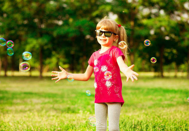 Mutlu küçük sarışın kız sabun köpüğü yaz parkta darbeler. - Fotoğraf, Görsel