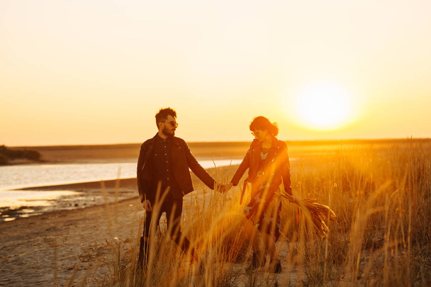 Enjoying time together.  Stylish and loving couple enjoying each other by the sea. The couple is young and in love. The concept of youth, love and lifestyle. Beautiful sunset on a summer day. - Foto, immagini
